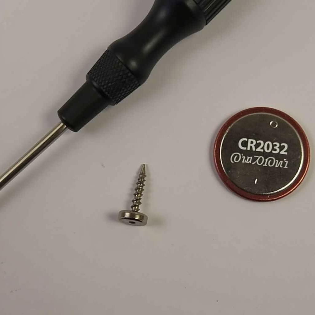 Tools and supplies for replacing a Cadillac key fob battery: a CR2032 battery and a small flathead screwdriver.